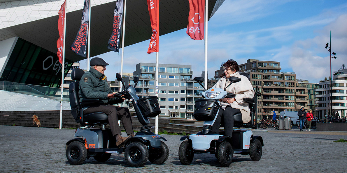 Twee gebruikers op Excel Galaxy EVO scootmobielen in stedelijke omgeving, comfortabel en zelfstandig onderweg
