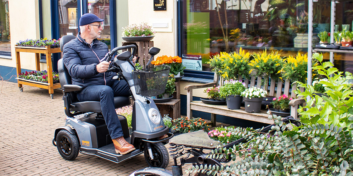 Gebruiker op een Excel Galaxy EVO scootmobiel tijdens een rit door een winkelstraat, comfortabel en zelfstandig onderweg