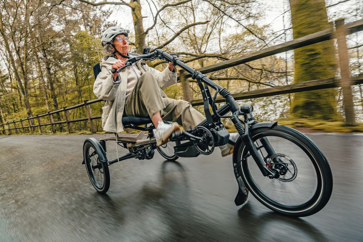 Vrouw fietst op een Hase Kettwiesel One ligdriewielfiets met elektrische ondersteuning op een verharde weg.